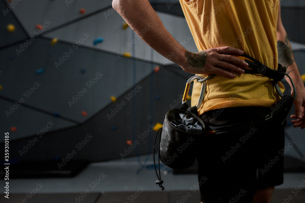 Cropped shot of sportive man, rock climber with a bag of magnesia, chalk. Training on the artificial climbing wall. Concept of sport life and rock climbing Cropped shot of sportive man, rock climber with a bag of magnesia, chalk. Training on the artificial climbing wall. Concept of sport life and rock climbing