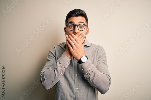 Young handsome man wearing elegant shirt and glasses over isolated white background shocked covering mouth with hands for mistake. Secret concept.