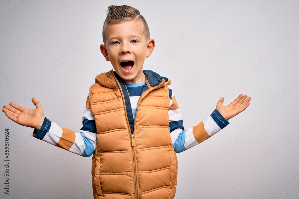 Young little caucasian kid with blue eyes standing wearing winter coat over isolated background celebrating crazy and amazed for success with arms raised and open eyes screaming excited. Young little caucasian kid with blue eyes standing wearing winter coat over isolated background celebrating crazy and amazed for success with arms raised and open eyes screaming excited.
