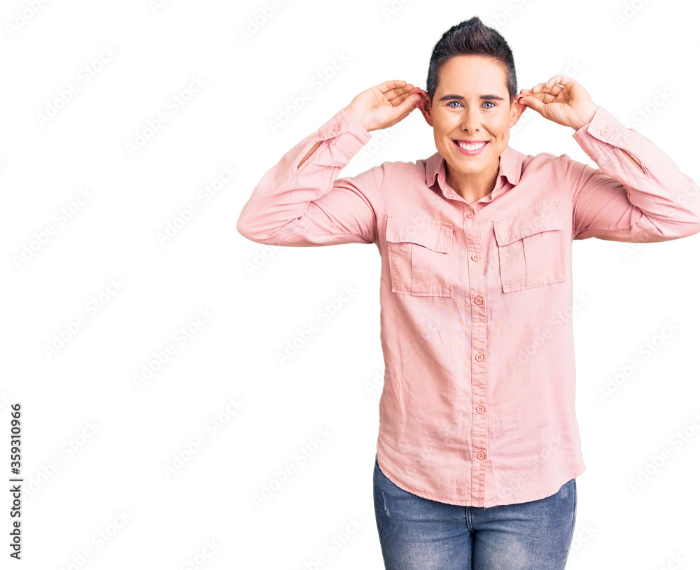 Fototapeta premium Young woman with short hair wearing casual clothes smiling pulling ears with fingers, funny gesture. audition problem