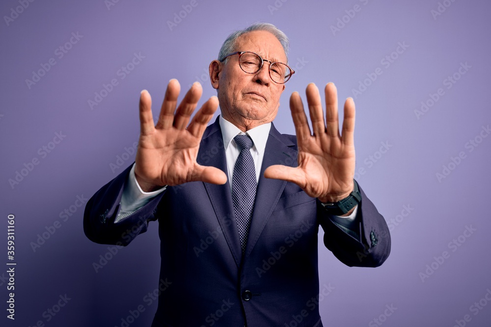 Grey haired senior business man wearing glasses and elegant suit and tie over purple background doing frame using hands palms and fingers, camera perspective Grey haired senior business man wearing glasses and elegant suit and tie over purple background doing frame using hands palms and fingers, camera perspective