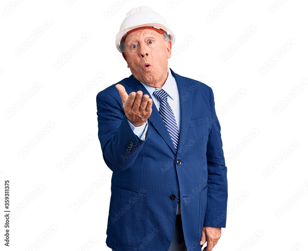 Senior handsome grey-haired man wearing suit and architect hardhat looking at the camera blowing a kiss with hand on air being lovely and sexy. love expression. Senior handsome grey-haired man wearing suit and architect hardhat looking at the camera blowing a kiss with hand on air being lovely and sexy. love expression.