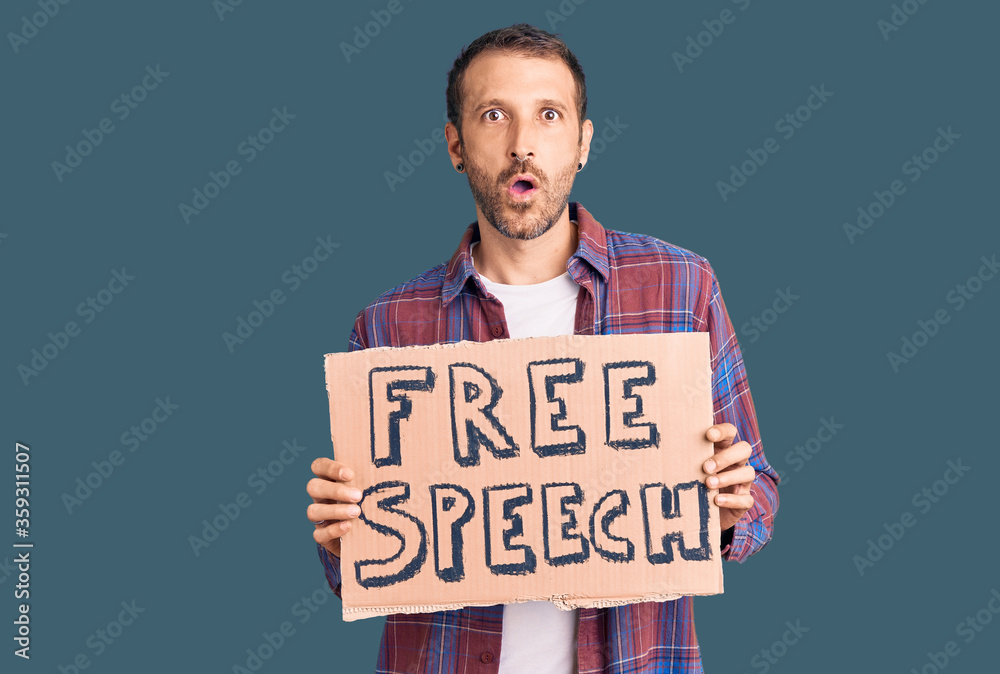 Young handsome man holding free speech banner scared and amazed with open mouth for surprise, disbelief face Young handsome man holding free speech banner scared and amazed with open mouth for surprise, disbelief face