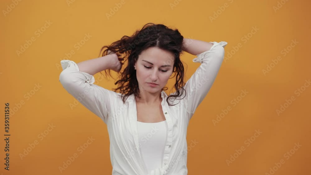 Teen smiling model brushing hand through hair, fashion posing, with hands in strand. Young attractive woman, dressed white blouse, with brown eyes, curly hair, yellow background Teen smiling model brushing hand through hair, fashion posing, with hands in strand. Young attractive woman, dressed white blouse, with brown eyes, curly hair, yellow background