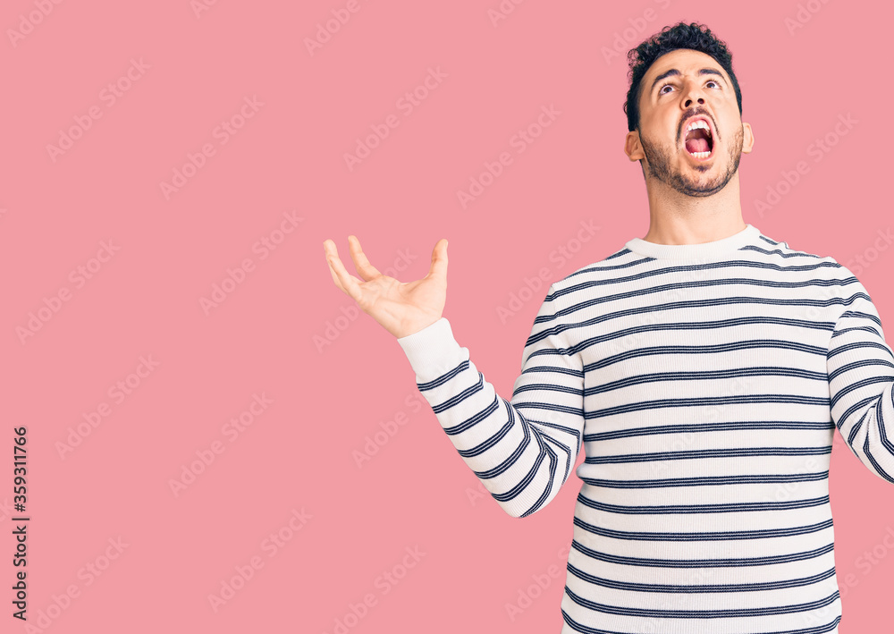 Young hispanic man wearing casual clothes crazy and mad shouting and yelling with aggressive expression and arms raised. frustration concept. Young hispanic man wearing casual clothes crazy and mad shouting and yelling with aggressive expression and arms raised. frustration concept.