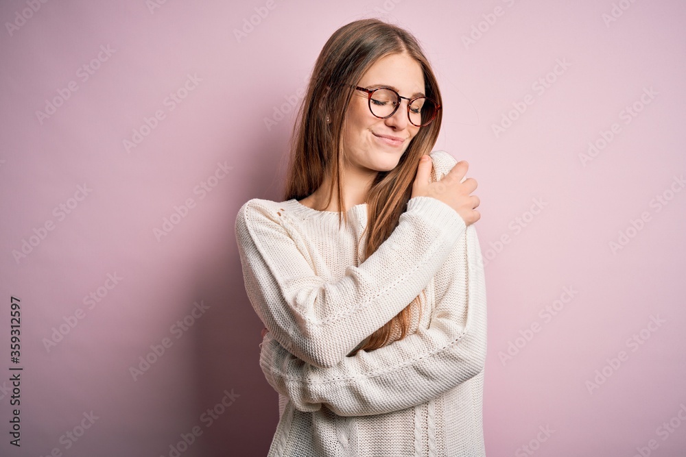 Young beautiful redhead woman wearing casual sweater and glasses over pink background Hugging oneself happy and positive, smiling confident. Self love and self care Young beautiful redhead woman wearing casual sweater and glasses over pink background Hugging oneself happy and positive, smiling confident. Self love and self care