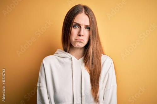 Young beautiful redhead sporty woman wearing sweatshirt over isolated yellow background depressed and worry for distress, crying angry and afraid. Sad expression.