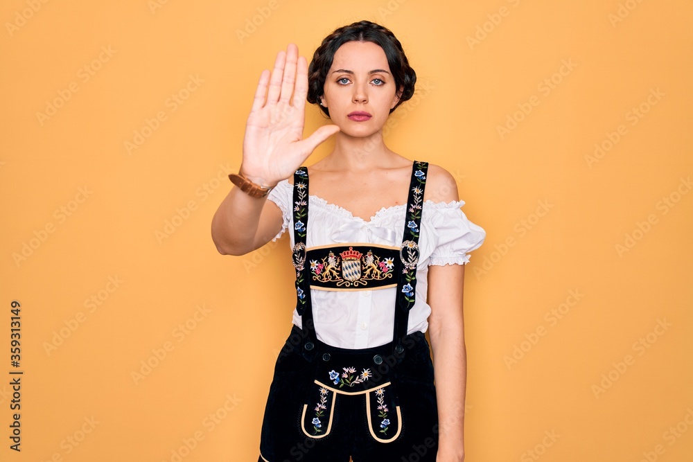 Young beautiful german woman with blue eyes wearing traditional octoberfest dress doing stop sing with palm of the hand. Warning expression with negative and serious gesture on the face. Young beautiful german woman with blue eyes wearing traditional octoberfest dress doing stop sing with palm of the hand. Warning expression with negative and serious gesture on the face.