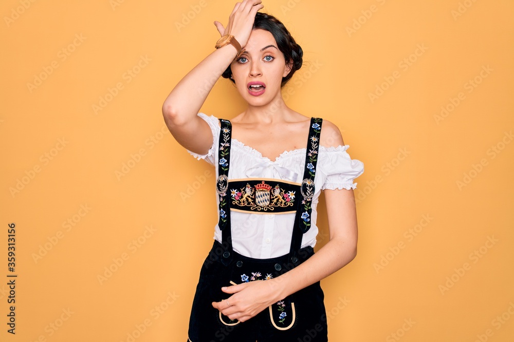 Young beautiful german woman with blue eyes wearing traditional octoberfest dress surprised with hand on head for mistake, remember error. Forgot, bad memory concept. Young beautiful german woman with blue eyes wearing traditional octoberfest dress surprised with hand on head for mistake, remember error. Forgot, bad memory concept.