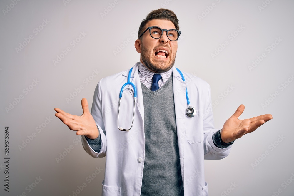 Young doctor man with blue eyes wearing medical coat and stethoscope over isolated background crazy and mad shouting and yelling with aggressive expression and arms raised. Frustration concept. Young doctor man with blue eyes wearing medical coat and stethoscope over isolated background crazy and mad shouting and yelling with aggressive expression and arms raised. Frustration concept.