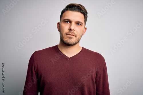 Young man with blue eyes wearing casual sweater standing over isolated background with serious expression on face. Simple and natural looking at the camera. © Krakenimages.com