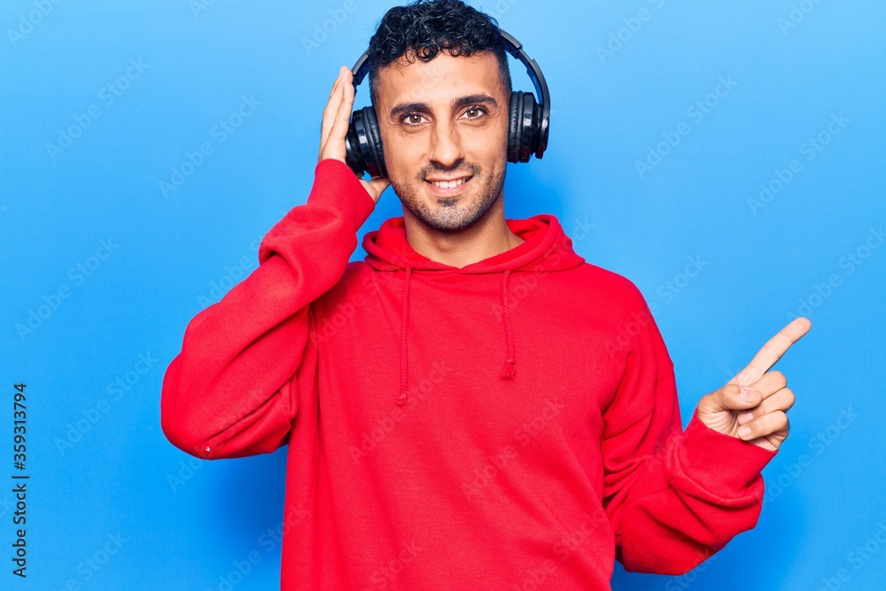 Naklejka premium Young hispanic man listening to music using headphones smiling happy pointing with hand and finger to the side