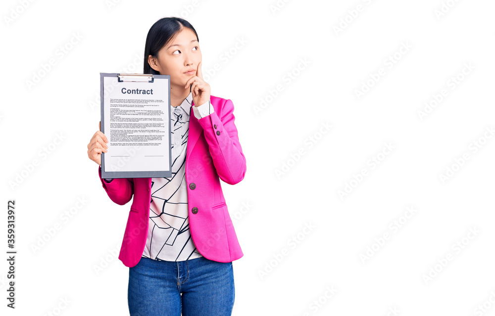 Young beautiful chinese woman holding clipboard with contract document serious face thinking about question with hand on chin, thoughtful about confusing idea Young beautiful chinese woman holding clipboard with contract document serious face thinking about question with hand on chin, thoughtful about confusing idea