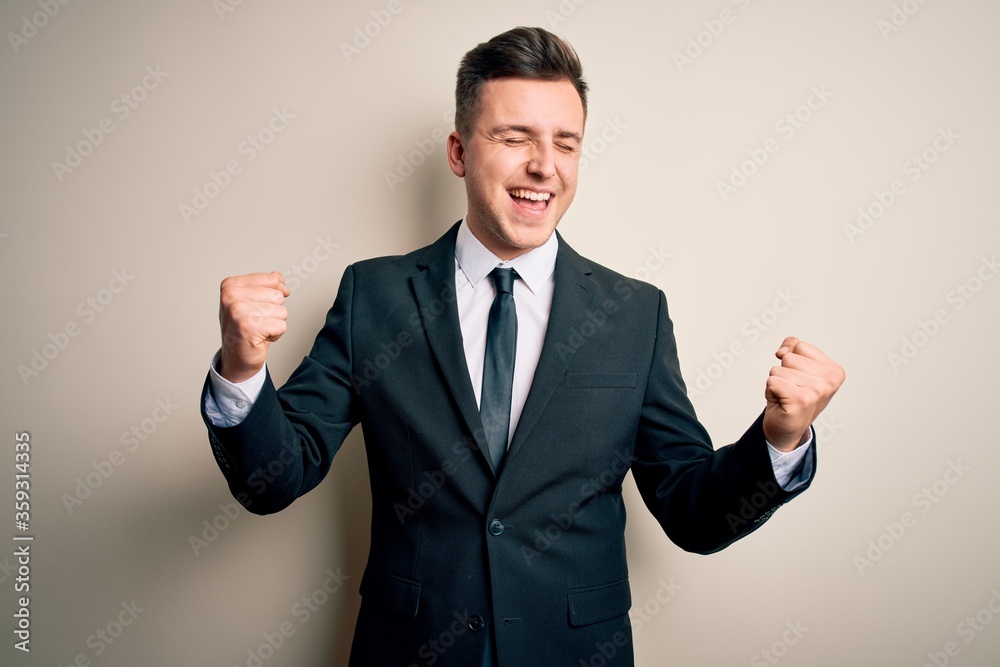Young handsome business man wearing elegant suit and tie over isolated background very happy and excited doing winner gesture with arms raised, smiling and screaming for success. Celebration concept. Young handsome business man wearing elegant suit and tie over isolated background very happy and excited doing winner gesture with arms raised, smiling and screaming for success. Celebration concept.