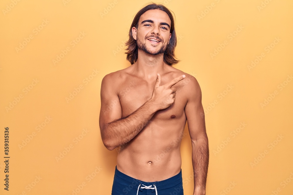 Young handsome man wearing swimwear shirtless smiling cheerful pointing with hand and finger up to the side
