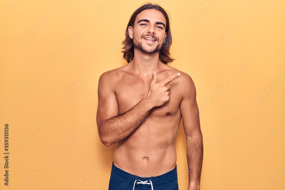 Fototapeta premium Young handsome man wearing swimwear shirtless smiling cheerful pointing with hand and finger up to the side