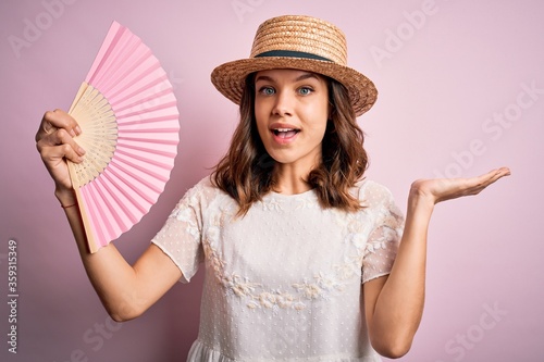 Young blonde fashion girl using wooden spanish hand fan on a hot summer day very happy and excited, winner expression celebrating victory screaming with big smile and raised hands