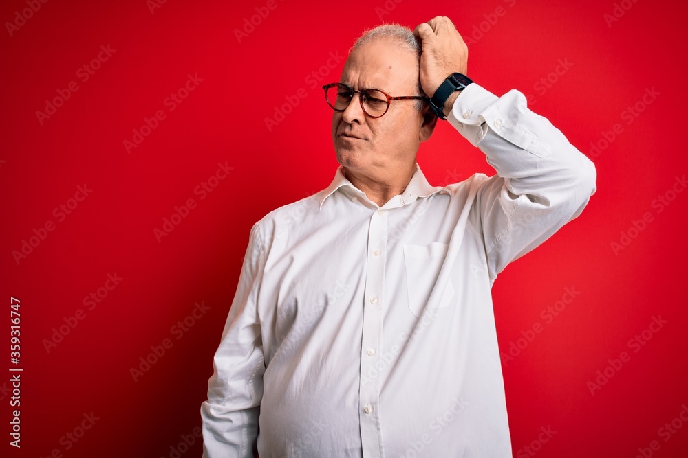 Fototapeta premium Middle age handsome hoary man wearing casual shirt and glasses over red background confuse and wondering about question. Uncertain with doubt, thinking with hand on head. Pensive concept.