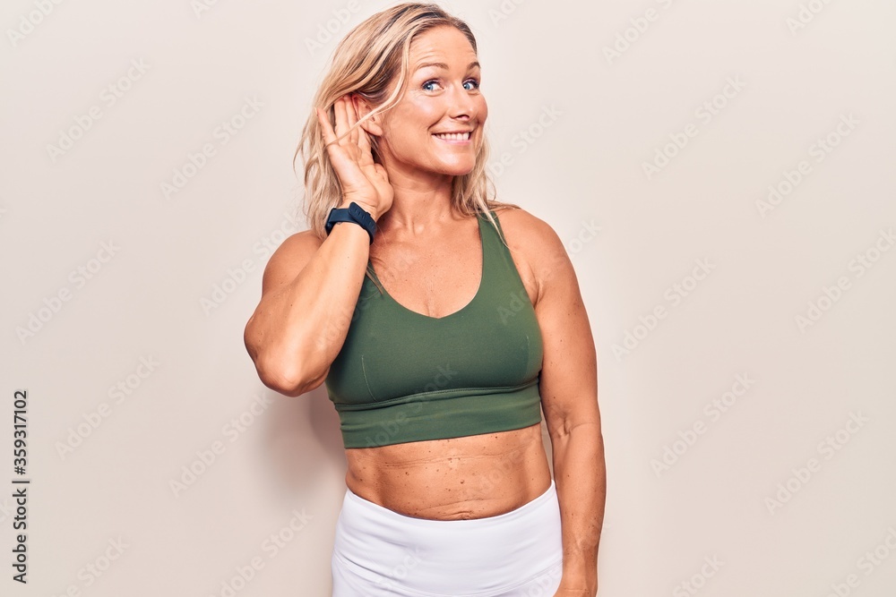 Middle age caucasian blonde woman wearing sportswear smiling with hand over ear listening an hearing to rumor or gossip. deafness concept. Middle age caucasian blonde woman wearing sportswear smiling with hand over ear listening an hearing to rumor or gossip. deafness concept.