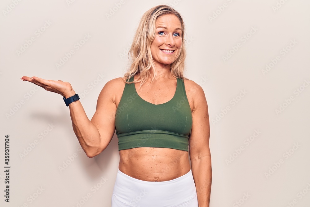 Middle age caucasian blonde woman wearing sportswear smiling cheerful presenting and pointing with palm of hand looking at the camera. Middle age caucasian blonde woman wearing sportswear smiling cheerful presenting and pointing with palm of hand looking at the camera.