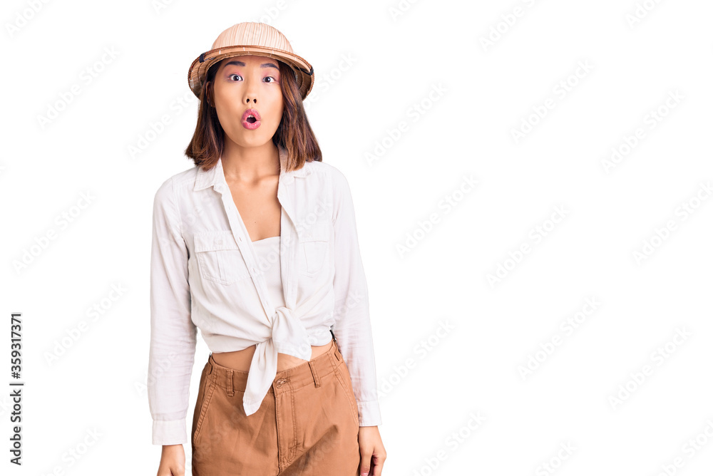 Young beautiful chinese girl wearing explorer hat scared and amazed with open mouth for surprise, disbelief face Young beautiful chinese girl wearing explorer hat scared and amazed with open mouth for surprise, disbelief face