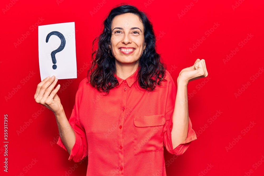 Young beautiful hispanic woman holding question mark screaming proud, celebrating victory and success very excited with raised arm Young beautiful hispanic woman holding question mark screaming proud, celebrating victory and success very excited with raised arm