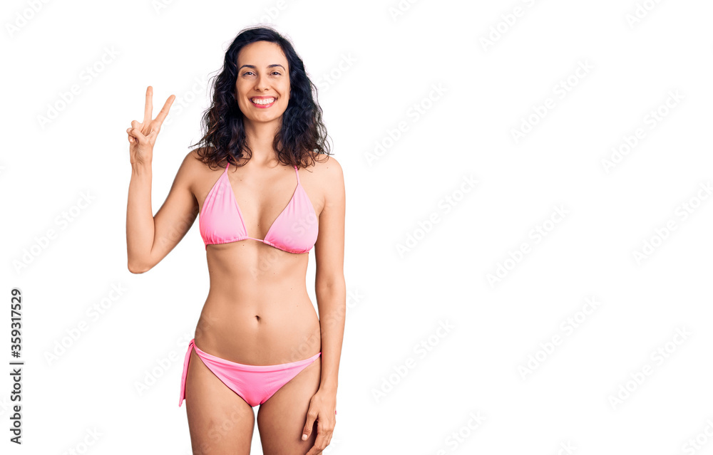 Young beautiful hispanic woman wearing bikini showing and pointing up with fingers number two while smiling confident and happy. Young beautiful hispanic woman wearing bikini showing and pointing up with fingers number two while smiling confident and happy.
