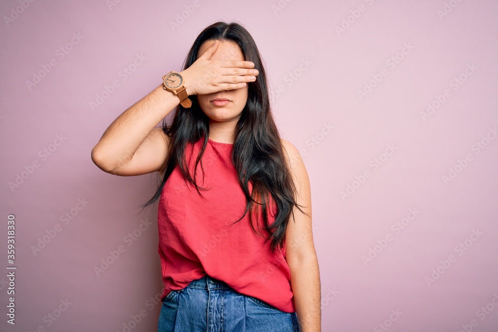 Young brunette woman wearing casual summer shirt over pink isolated background covering eyes with hand, looking serious and sad. Sightless, hiding and rejection concept Young brunette woman wearing casual summer shirt over pink isolated background covering eyes with hand, looking serious and sad. Sightless, hiding and rejection concept