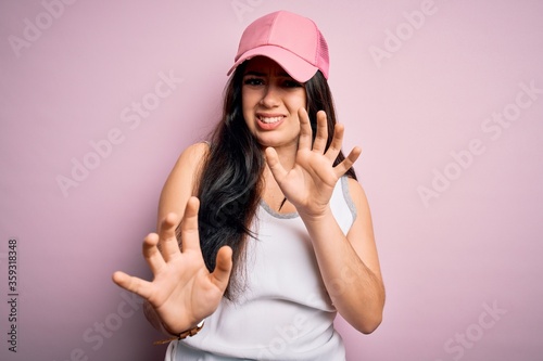 Young brunette woman wearing casual sport cap over pink background disgusted expression, displeased and fearful doing disgust face because aversion reaction. With hands raised © Krakenimages.com