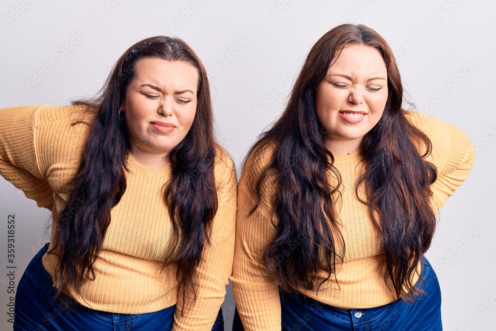 Young plus size twins wearing casual clothes suffering of backache, touching back with hand, muscular pain Young plus size twins wearing casual clothes suffering of backache, touching back with hand, muscular pain