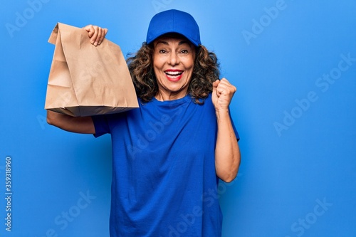 Middle age beautiful delivery woman holding deliver paper bag with takeaway food screaming proud, celebrating victory and success very excited with raised arm
