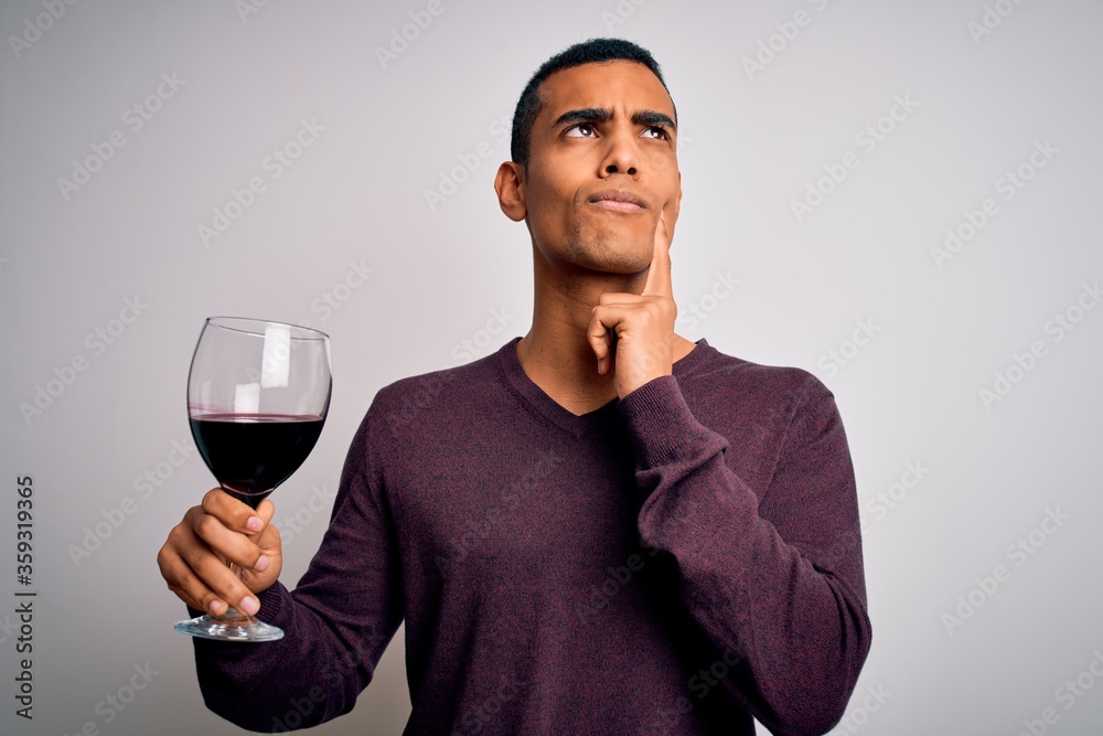 Handsome african american sommelier man tasting glass of red wine over white background serious face thinking about question, very confused idea Handsome african american sommelier man tasting glass of red wine over white background serious face thinking about question, very confused idea