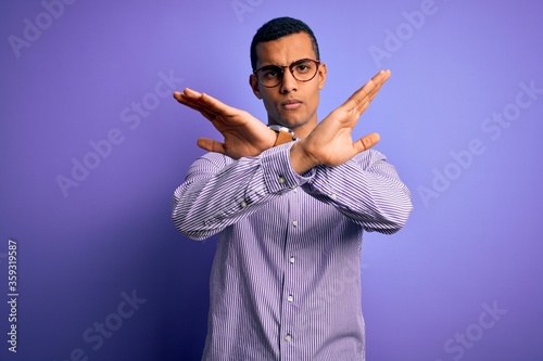 Handsome african american man wearing striped shirt and glasses over purple background Rejection expression crossing arms doing negative sign, angry face