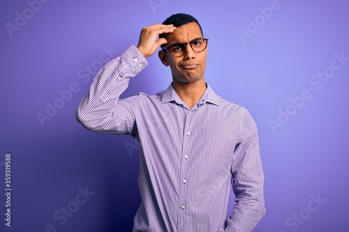 Handsome african american man wearing striped shirt and glasses over purple background worried and stressed about a problem with hand on forehead, nervous and anxious for crisis