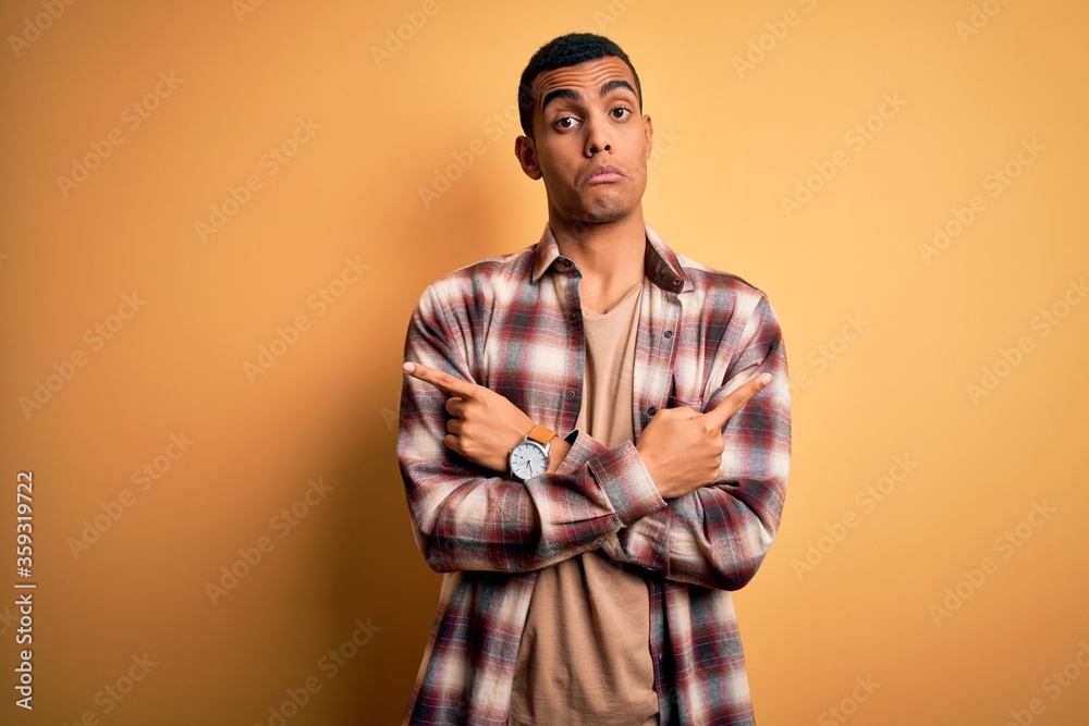 Young handsome african american man wearing casual shirt standing over yellow background Pointing to both sides with fingers, different direction disagree Young handsome african american man wearing casual shirt standing over yellow background Pointing to both sides with fingers, different direction disagree
