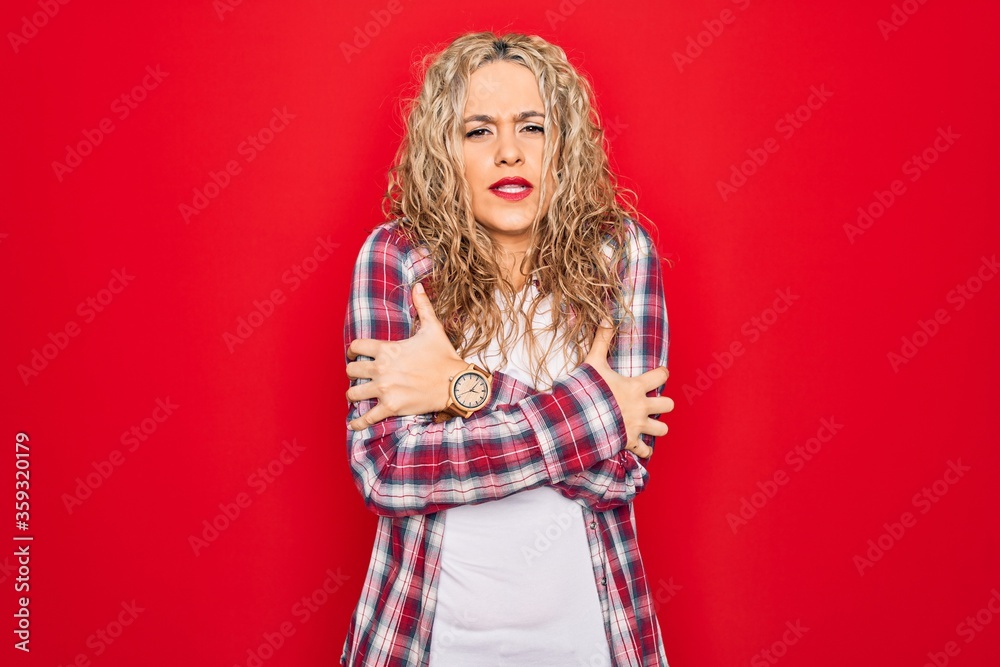 Young beautiful blonde woman wearing casual shirt standing over isolated red background shaking and freezing for winter cold with sad and shock expression on face