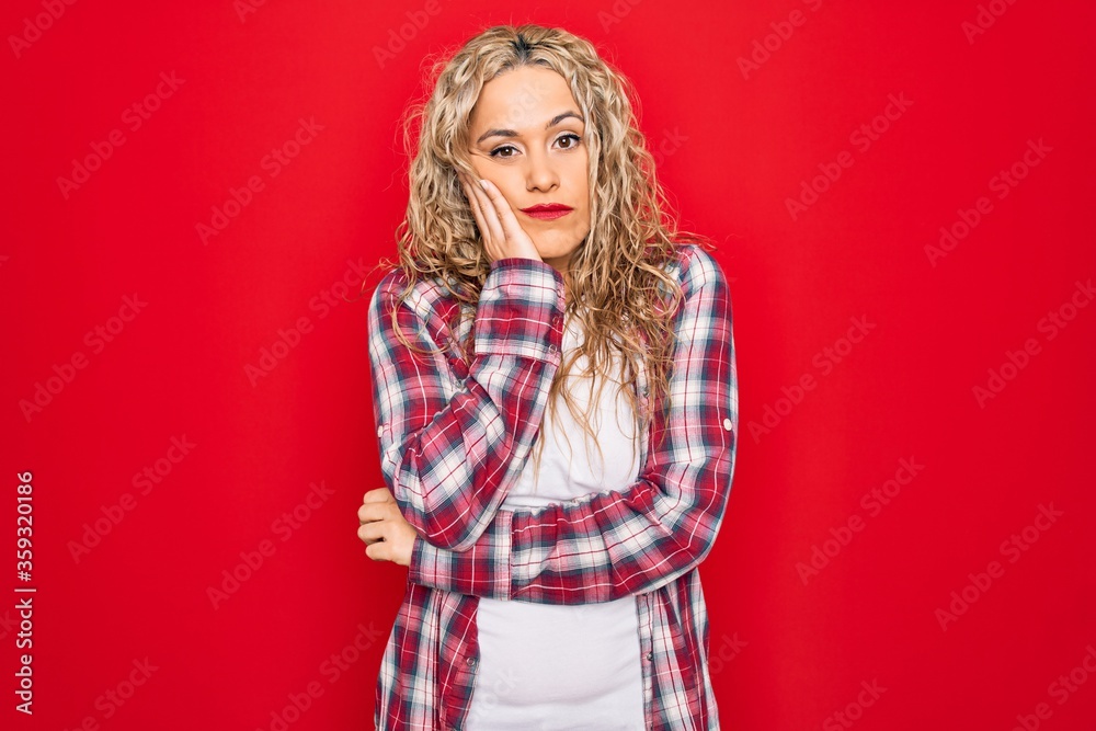 Young beautiful blonde woman wearing casual shirt standing over isolated red background thinking looking tired and bored with depression problems with crossed arms. Young beautiful blonde woman wearing casual shirt standing over isolated red background thinking looking tired and bored with depression problems with crossed arms.