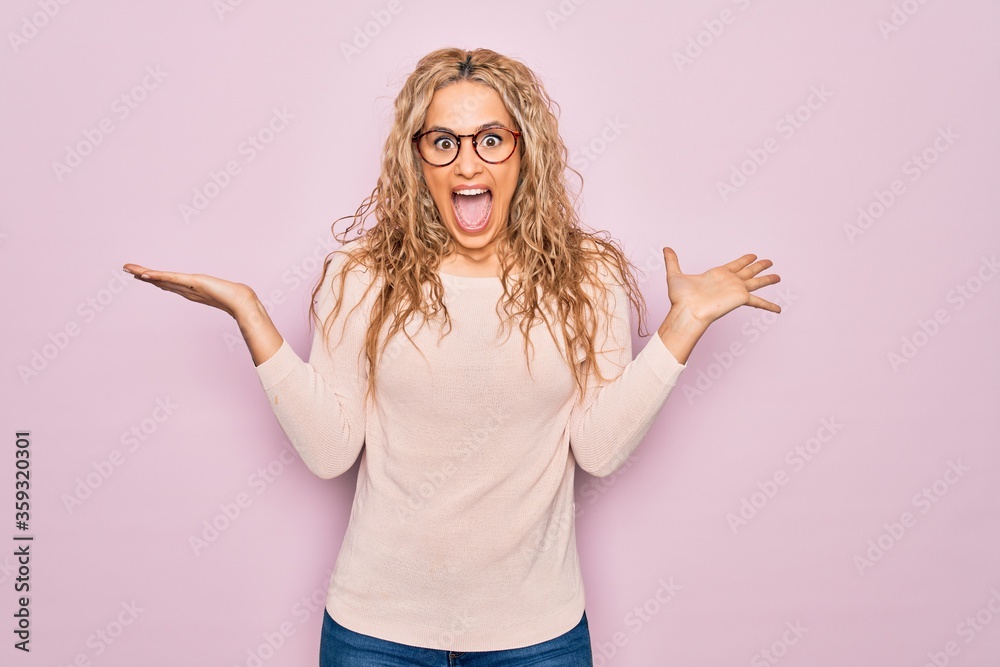 Φωτογραφία Young beautiful blonde woman wearing casual sweater and glasses over pink background celebrating crazy and amazed for success with arms raised and open eyes screaming excited