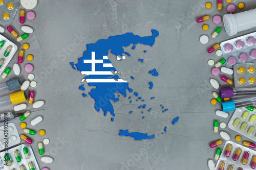 The Greece State began research for treatment and medicine to combat the pandemic outbreak disease coronavirus. Medicine, pills, needles, syringes and Greece map and flag on gray background.