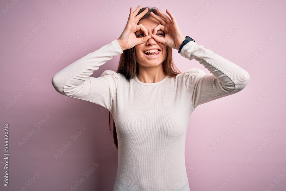 Young beautiful woman with blue eyes wearing casual white t-shirt over pink background doing ok gesture like binoculars sticking tongue out, eyes looking through fingers. Crazy expression. Young beautiful woman with blue eyes wearing casual white t-shirt over pink background doing ok gesture like binoculars sticking tongue out, eyes looking through fingers. Crazy expression.