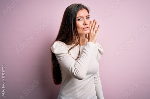 Young beautiful woman with blue eyes wearing casual white t-shirt over pink background hand on mouth telling secret rumor, whispering malicious talk conversation