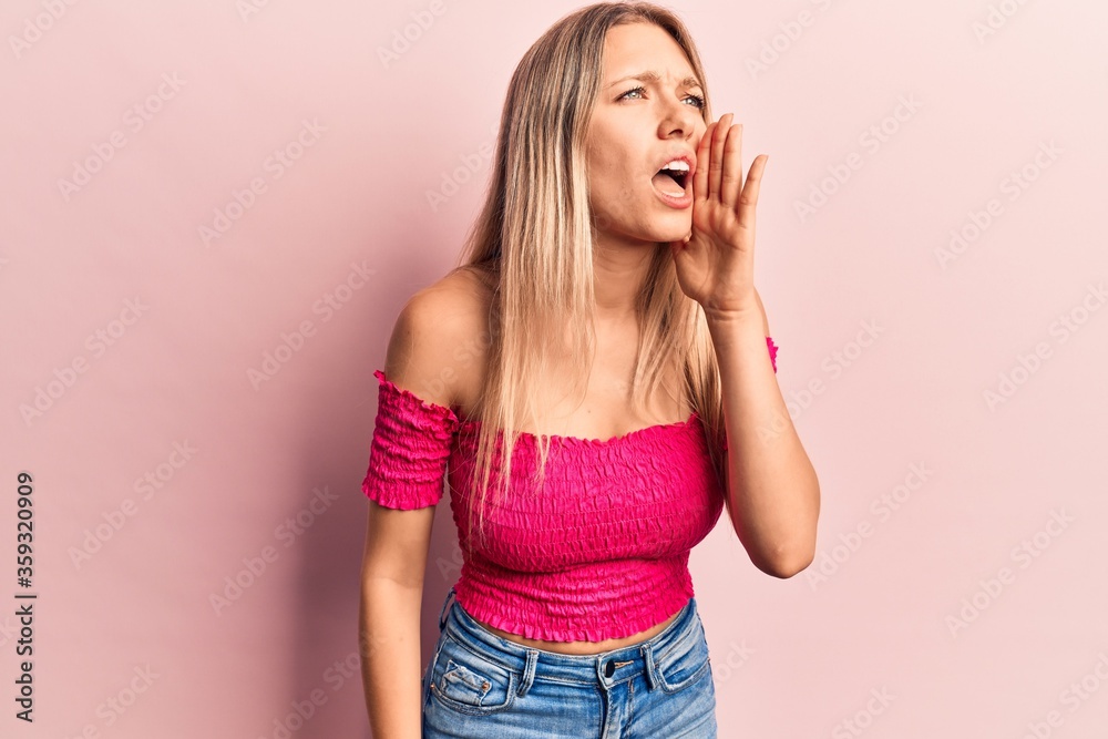 Young blonde woman wearing casual clothes shouting and screaming loud to side with hand on mouth. communication concept. Young blonde woman wearing casual clothes shouting and screaming loud to side with hand on mouth. communication concept.