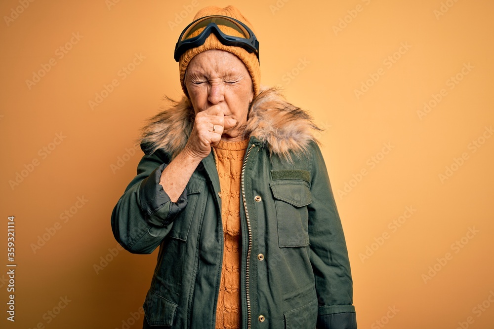 Senior beautiful grey-haired skier woman wearing snow sportswear and ski goggles feeling unwell and coughing as symptom for cold or bronchitis. Health care concept. Senior beautiful grey-haired skier woman wearing snow sportswear and ski goggles feeling unwell and coughing as symptom for cold or bronchitis. Health care concept.