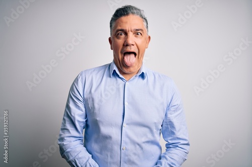 Middle age handsome grey-haired business man wearing elegant shirt over white background sticking tongue out happy with funny expression. Emotion concept. © Krakenimages.com