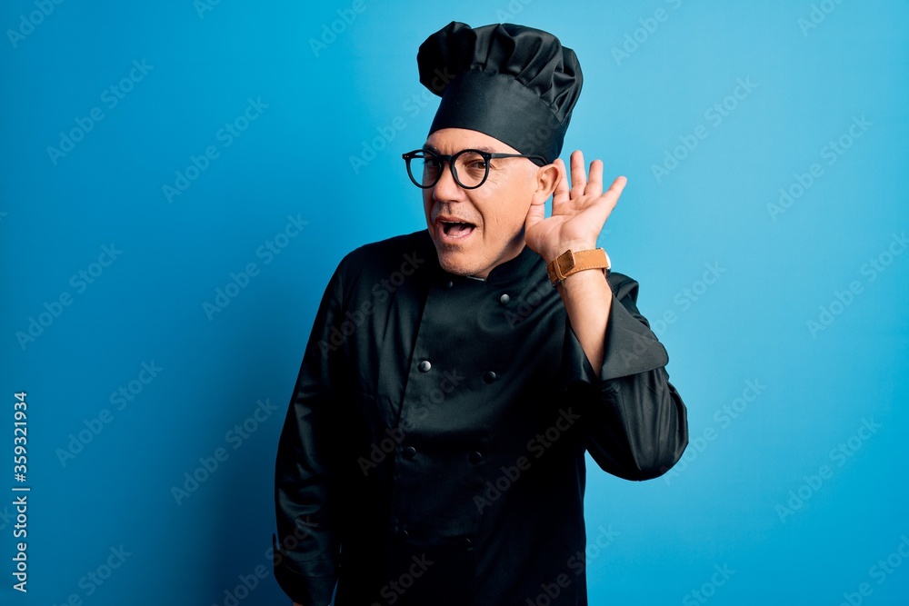 Middle age handsome grey-haired chef man wearing cooker uniform and hat smiling with hand over ear listening an hearing to rumor or gossip. Deafness concept. Middle age handsome grey-haired chef man wearing cooker uniform and hat smiling with hand over ear listening an hearing to rumor or gossip. Deafness concept.