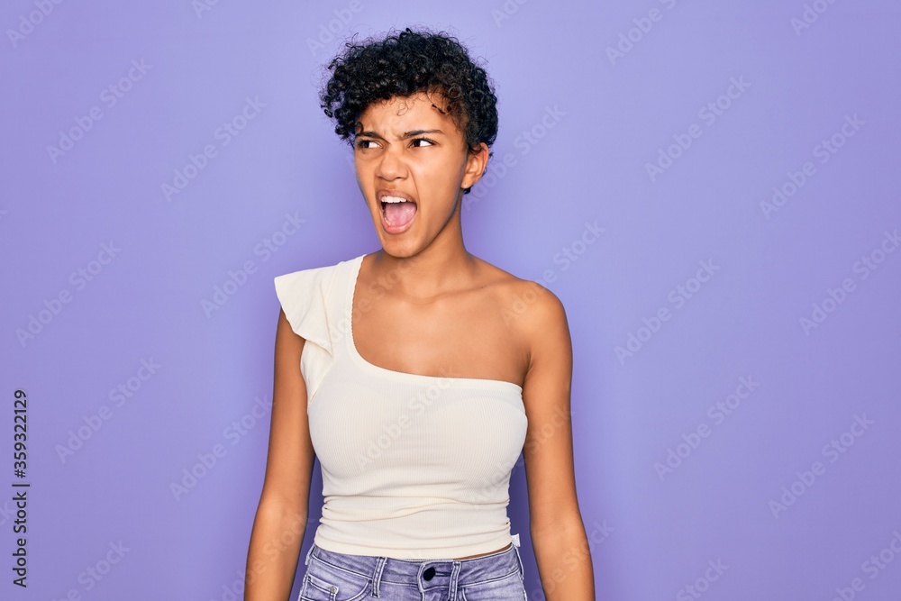 Young beautiful african american afro woman wearing casual t-shirt over purple background angry and mad screaming frustrated and furious, shouting with anger. Rage and aggressive concept. Young beautiful african american afro woman wearing casual t-shirt over purple background angry and mad screaming frustrated and furious, shouting with anger. Rage and aggressive concept.