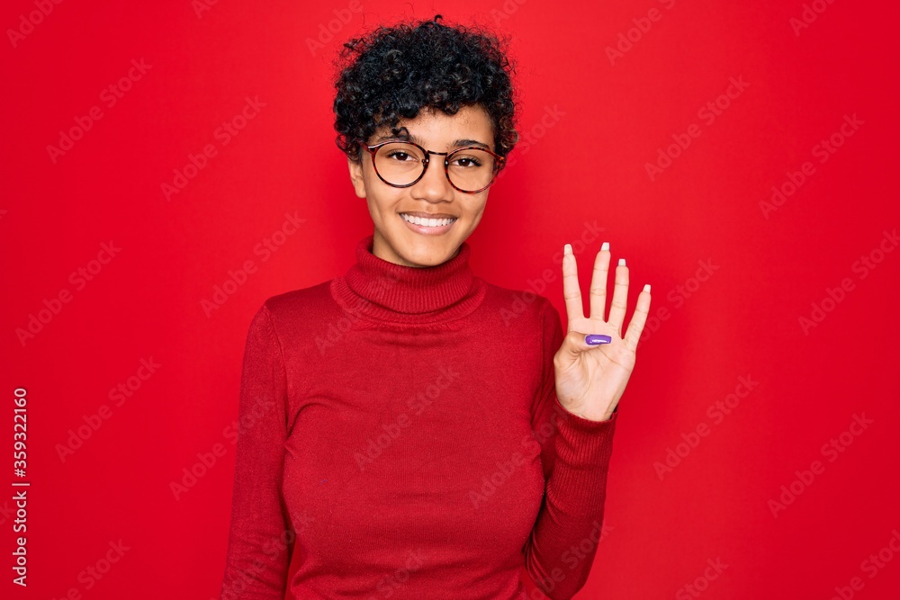 Naklejka premium Young beautiful african american afro woman wearing turtleneck sweater and glasses showing and pointing up with fingers number four while smiling confident and happy.