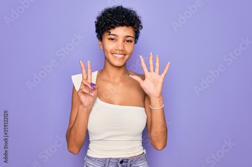 Young beautiful african american afro woman wearing casual t-shirt over purple background showing and pointing up with fingers number seven while smiling confident and happy.