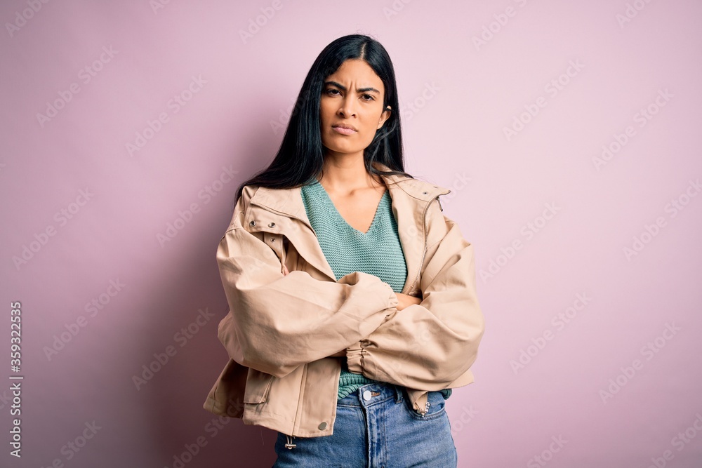Young beautiful hispanic fashion woman wearing winter jacket and sweater over pink background skeptic and nervous, disapproving expression on face with crossed arms. Negative person. Young beautiful hispanic fashion woman wearing winter jacket and sweater over pink background skeptic and nervous, disapproving expression on face with crossed arms. Negative person.
