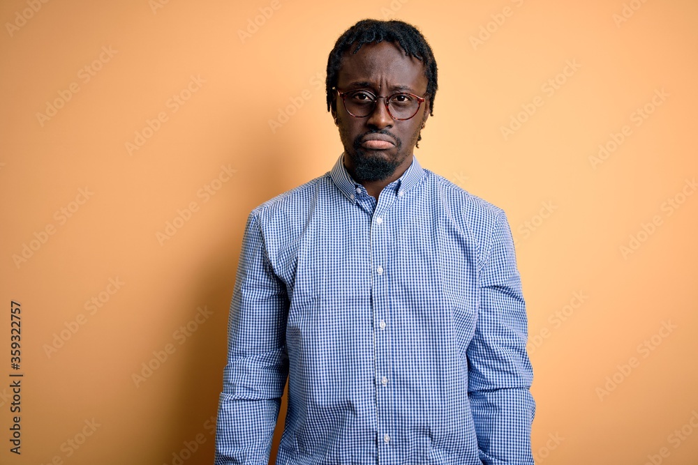 Young handsome african american man wearing shirt and glasses over yellow background depressed and worry for distress, crying angry and afraid. Sad expression. Young handsome african american man wearing shirt and glasses over yellow background depressed and worry for distress, crying angry and afraid. Sad expression.